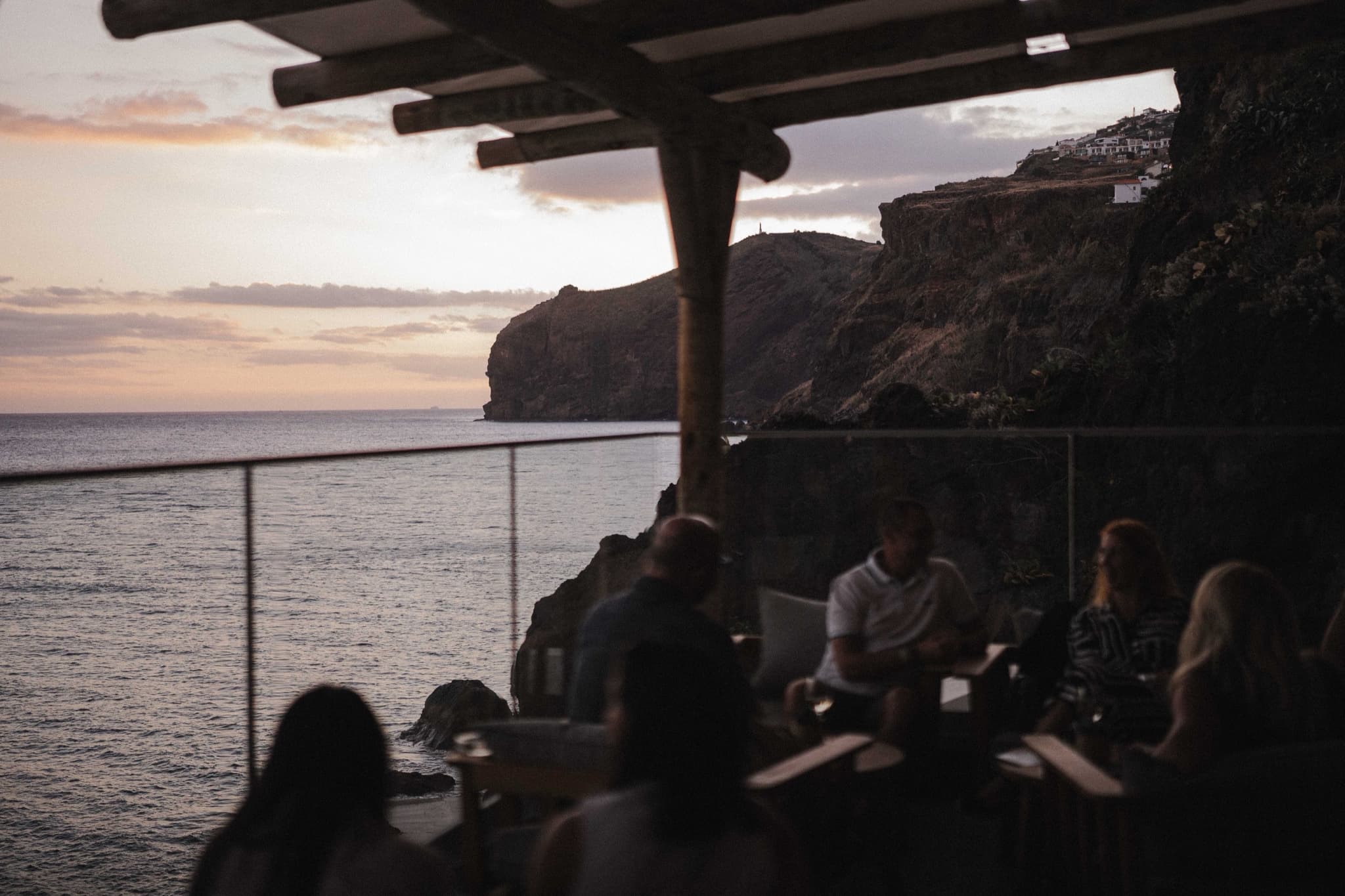 Friends talking over drinks on a cliffside terrace above the sea at sunset